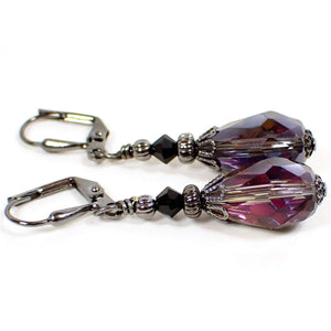 Side view of the handmade teardrop earrings. The metal is gunmetal gray in color. There are black faceted glass beads at the top. The bottom teardrop beads are vitrail style with dark metallic gray on one side and flashes of mostly pink and purple on the inside of the other side as they catch the light.