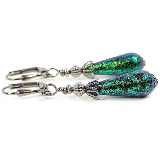 Side view of the handmade glitter drop earrings. The metal is gunmetal gray in color. There are black vintage teardrop beads on the bottom that have green glitter on the outside of them.