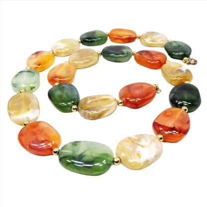 Front view of the retro vintage lucite beaded necklace. The are flat freeform shape beads. There are beads with marbled shades of orange, yellow, and green with small gold tone metal beads in between.