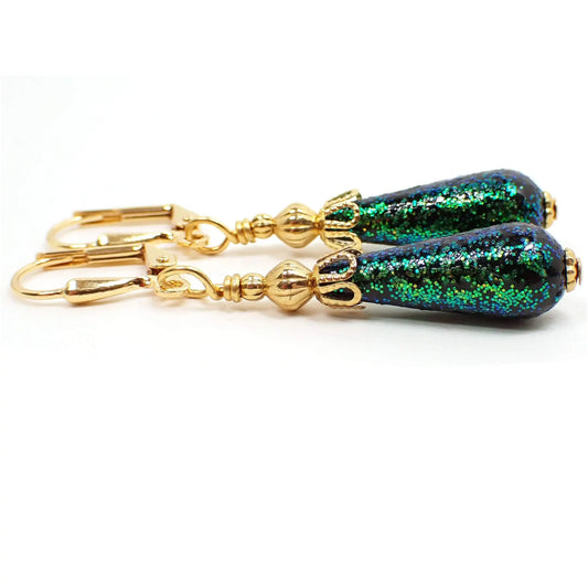 Angled side view of the handmade small teardrop earrings. They have gold plated color metal with small black vintage acrylic teardrop beads at the bottom that have bright green glitter embedded in them.