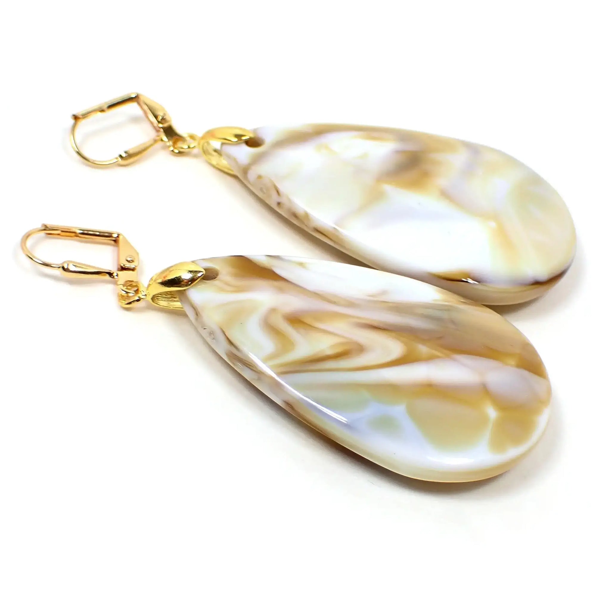 Angled view of the handmade acrylic large teardrop earrings. The metal is gold tone plated in color. They are large puffy teardrop shaped and are white with yellow and brown marbled in.