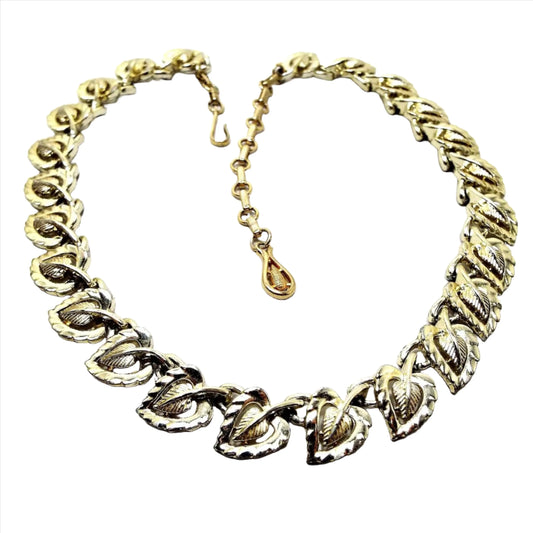 Front view of the Mid Century vintage Coro link necklace. It is gold tone in color with a hook end clasp. Each link has an angled and textured leaf shape with the largest ones at the bottom of the necklace.