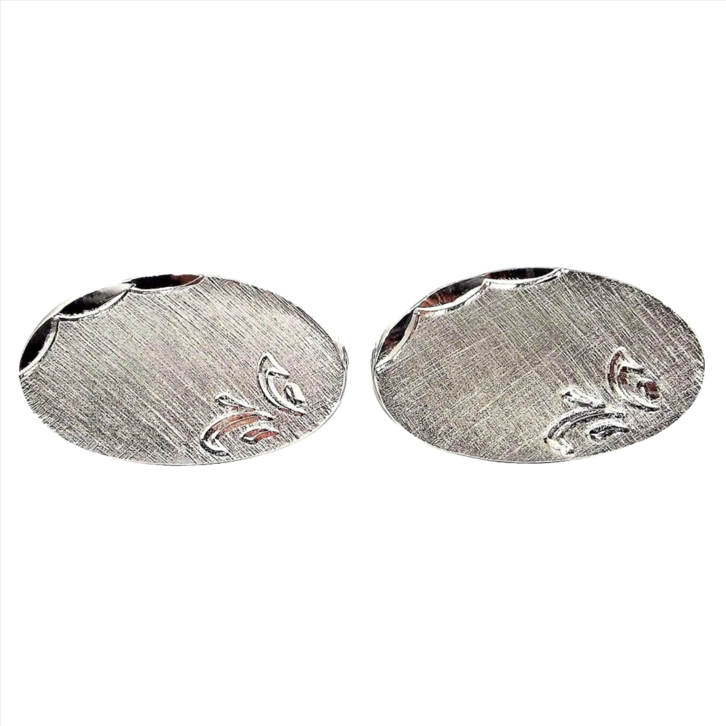 Front view of the Mid Century vintage Shields cufflinks. They are silver tone in color with matte brushed fronts. There is a faceted edge on the top side and a leaf like design etched on the other corner. They are shaped like ovals.