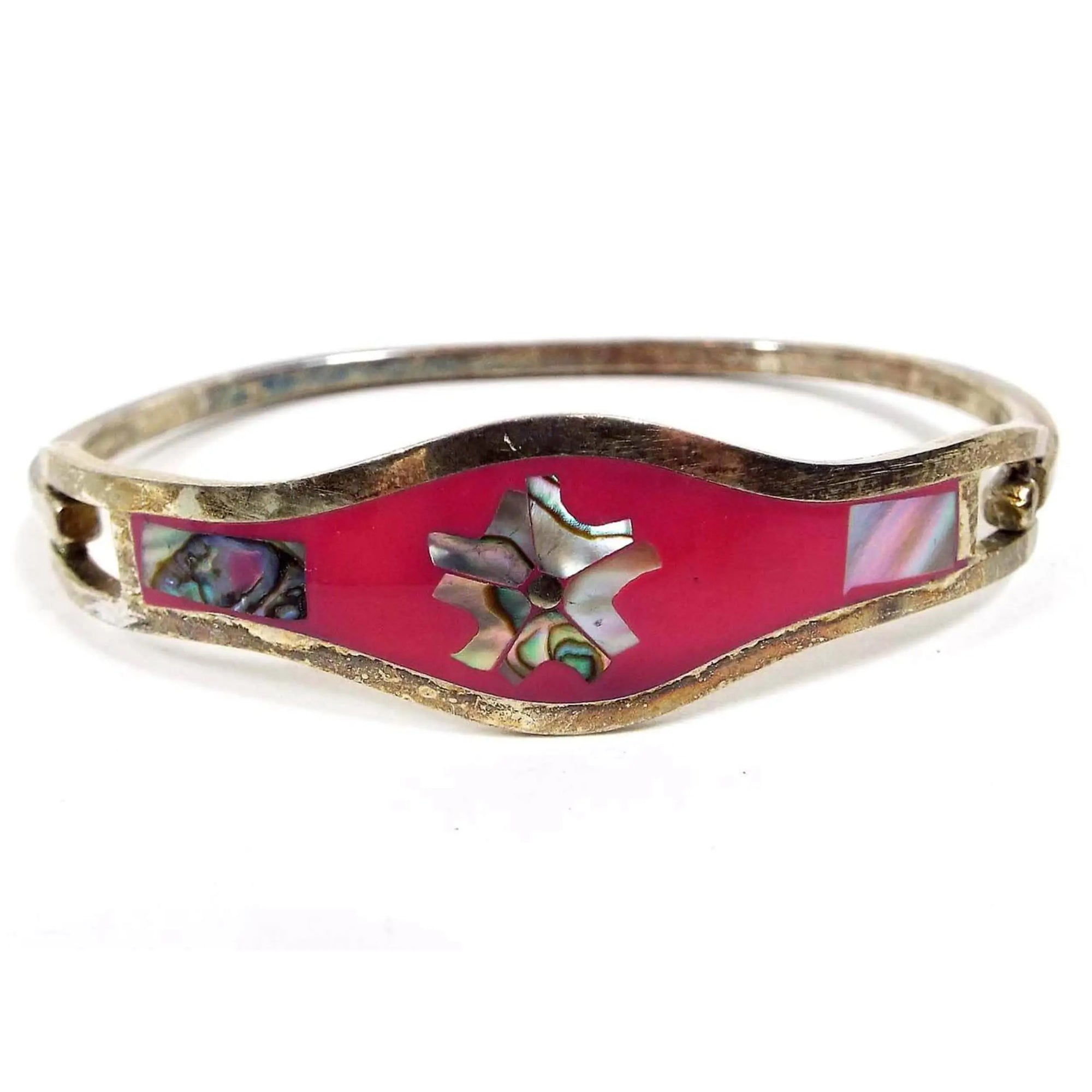 Front view of the retro vintage abalone floral hinged bangle bracelet. The front has a rounded middle area with bright pink enamel and inlaid abalone shell in a flower shape. There is a rectangle piece of abalone at each side as well. The metal is darkened silver tone color from age.