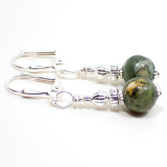 Enlarged view of the handmade rainforest jasper earrings. The metal is silver plated in color. There are small faceted black crystal bicone beads at the top. The bottom gemstone beads are round sphere shaped and have marbled shades of green, peach, and white.