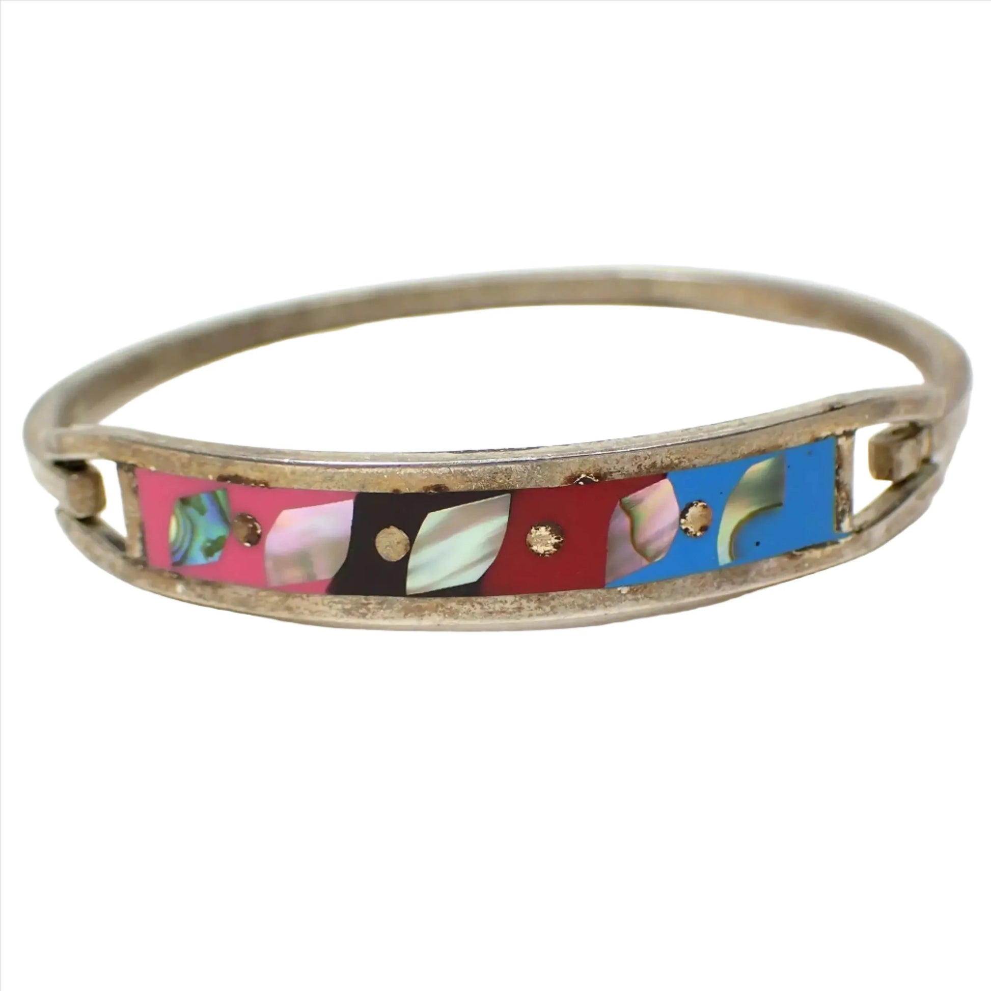 Front view of the retro vintage hinged bangle bracelet made in Mexico. The metal is darkened silver tone in color. There is a curved band on the front with pink, black, red, and blue resin that has small pieces of inlaid abalone shell in them.
