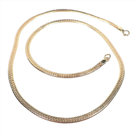 Top view of the retro vintage Krementz herringbone chain necklace. It is gold tone in color and has a flat herringbone link design. There is a spring ring clasp at one end and a ring at the other end that has markings on it.