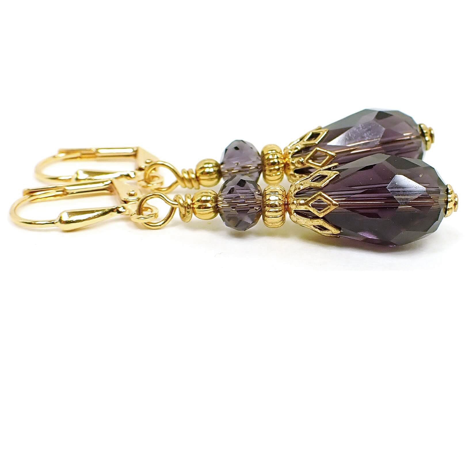 Side view of the handmade teardrop earrings. The metal is gold plated in color. The beads are faceted glass crystal in a grape candy color. The bottom beads are teardrop shaped.