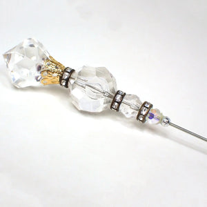 Enlarged view of the top of the Mid Century vintage hat pin. There is a clear plastic faceted top with a point at the top that has a filigree gold tone bead cap at the bottom of it. There are three faceted round clear plastic beads below that going down in size as you go down the pin. Each bead is separated with an antiqued copper tone disc bead that has clear round rhinestones all the way around it. The pin is silver tone plated in color.