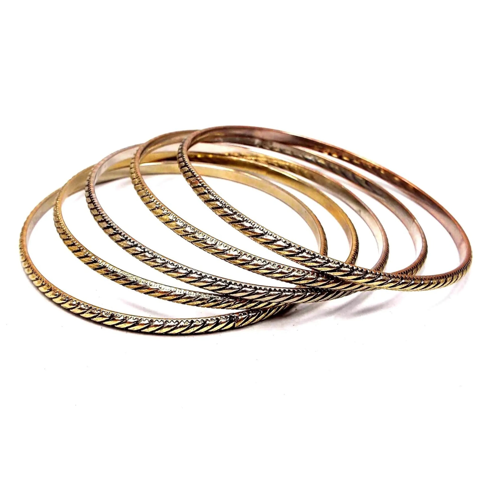 Angled view of the stack of five retro vintage bangle bracelets. They are gold tone in color with black diagonal lines. Each is thinner in width to make them good for stacking together.