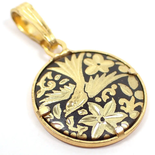 Enlarged top view of the retro vintage small Damascene charm pendant. It is gold tone plated in color and round. There is a bird in the middle with a floral design around it and a black background.