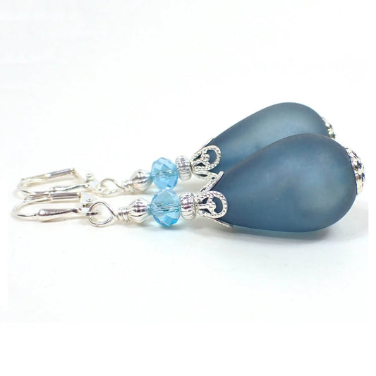 Side view of the large handmade earrings with vintage lucite beads. The metal is silver plated in color. There are faceted light blue glass crystals at the top. The bottom vintage lucite beads are large plump teardrop shaped and have a frosted country blue color.
