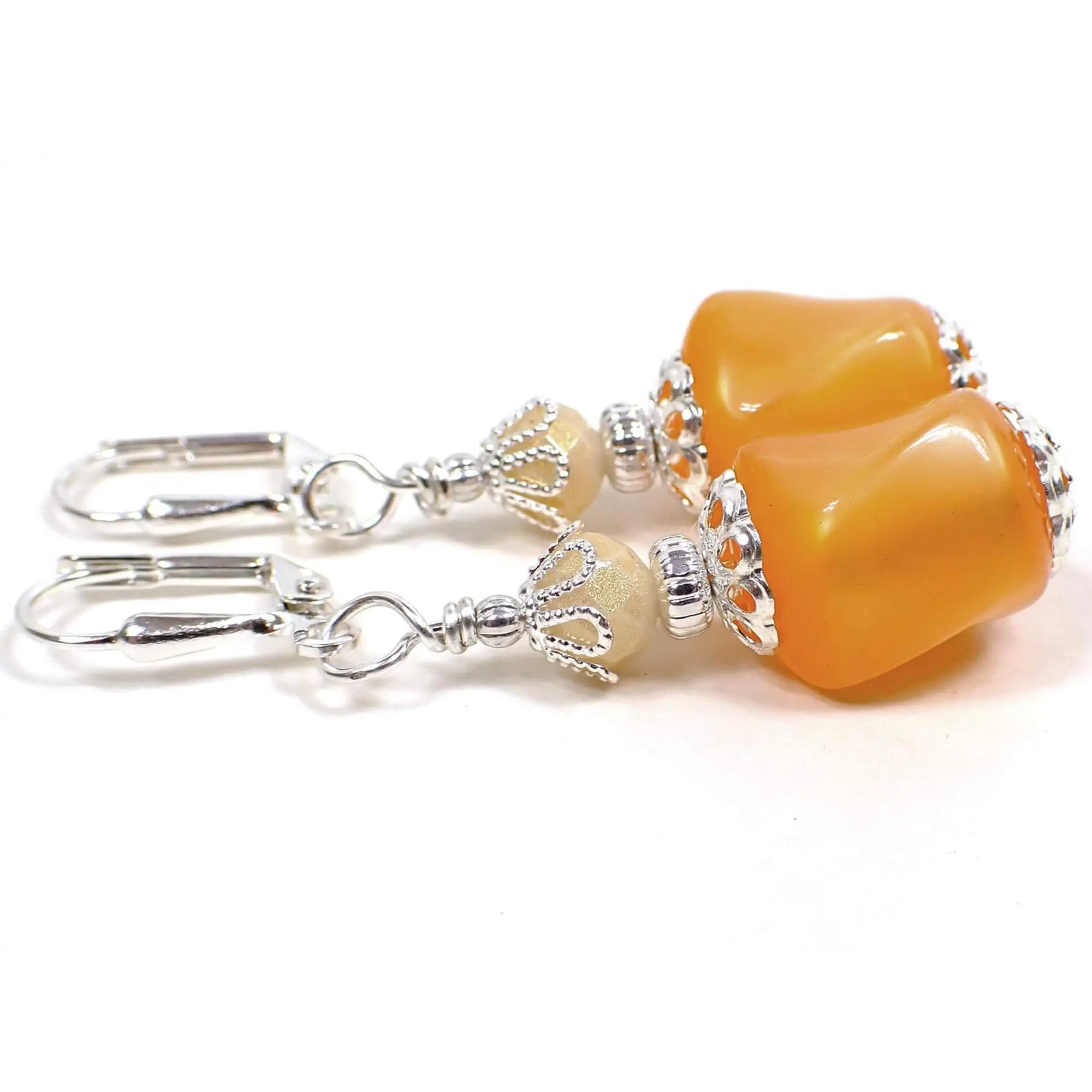Side view of the handmade earrings with vintage moonglow lucite beads. The metal is silver plated in color. There are new faceted glass beads at the top with a golden sheen color on them. The bottom vintage beads are twisted barrel shaped moonglow lucite in a citrus peach orange color. There is an inner like glow as you move around in the light.