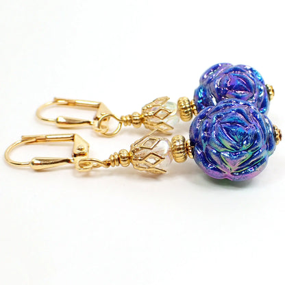top view of the handmade flower earrings with AB blue acrylic beads. The metal is gold plated in color. The top beads are AB clear faceted ovals. The bottom beads are shaped like flowers and are primarily blue with AB coating that gives flashes of other colors like pink and green and purple as you move around in the light.