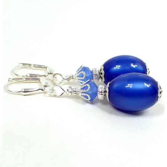 Side view of the handmade drop earrings. The metal is silver plated in color. There are faceted glass beads at the top in light blue. The bottom beads are oval vintage moonglow lucite beads in a vibrant blue color. They have an inside glow like appearance when you move around in the light.