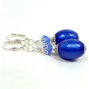 Side view of the handmade drop earrings. The metal is silver plated in color. There are faceted glass beads at the top in light blue. The bottom beads are oval vintage moonglow lucite beads in a vibrant blue color. They have an inside glow like appearance when you move around in the light.