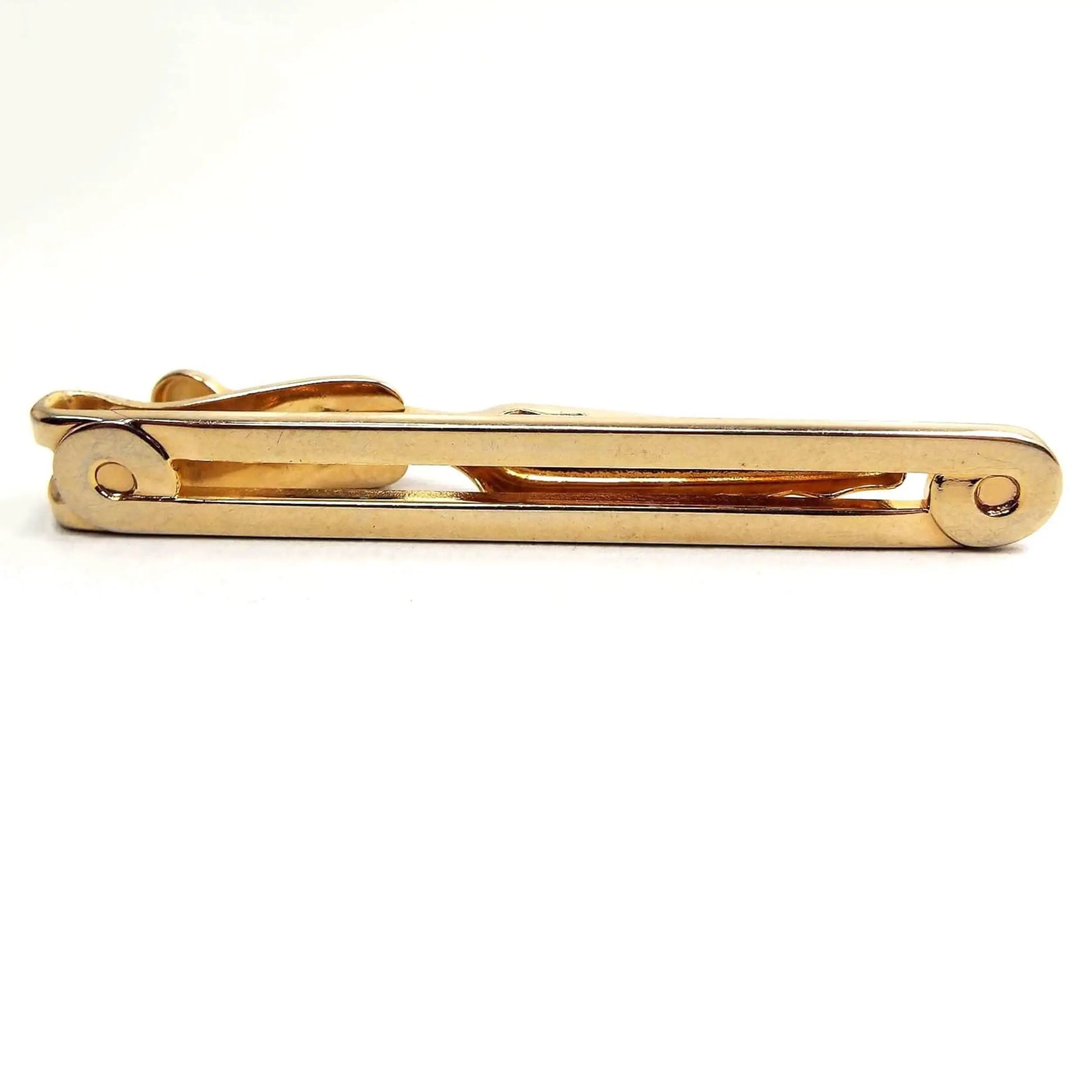 Front view of the Mid Century vintage long Swank tie clip. It is gold tone in color. It is long bar shaped with an open middle and curled end design.