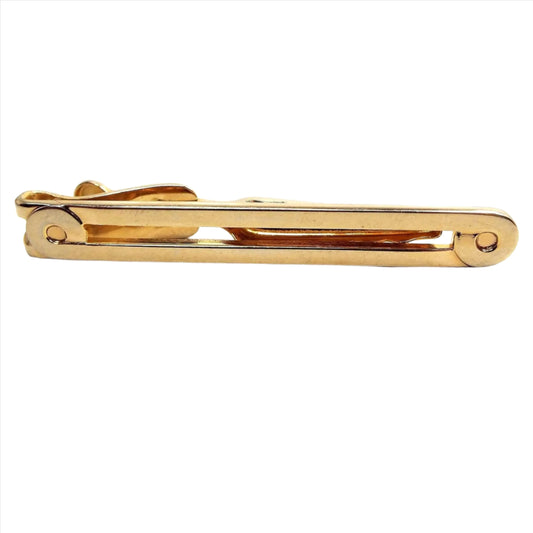 Front view of the Mid Century vintage long Swank tie clip. It is gold tone in color. It is long bar shaped with an open middle and curled end design.