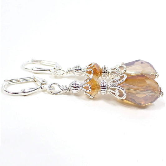 Side view of the handmade teardrop earrings. The metal is silver plated in color. There are faceted glass crystal rondelle beads on top and teardrop beads on the bottom. The beads have a light peach color with an opalescent white color combo.