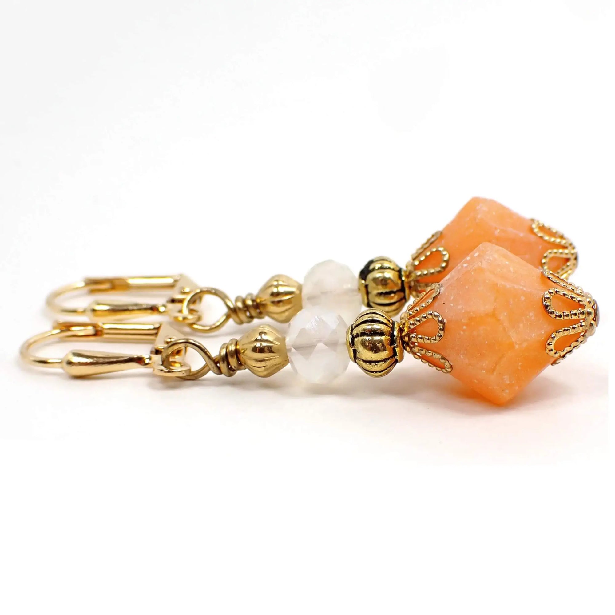 Side view of the handmade bicone acrylic drop earrings. The metal is gold plated in color. There are faceted glass beads at the top in a semi translucent white color. The bottom acrylic beads are bicone shaped and are a frosted matte peach color.