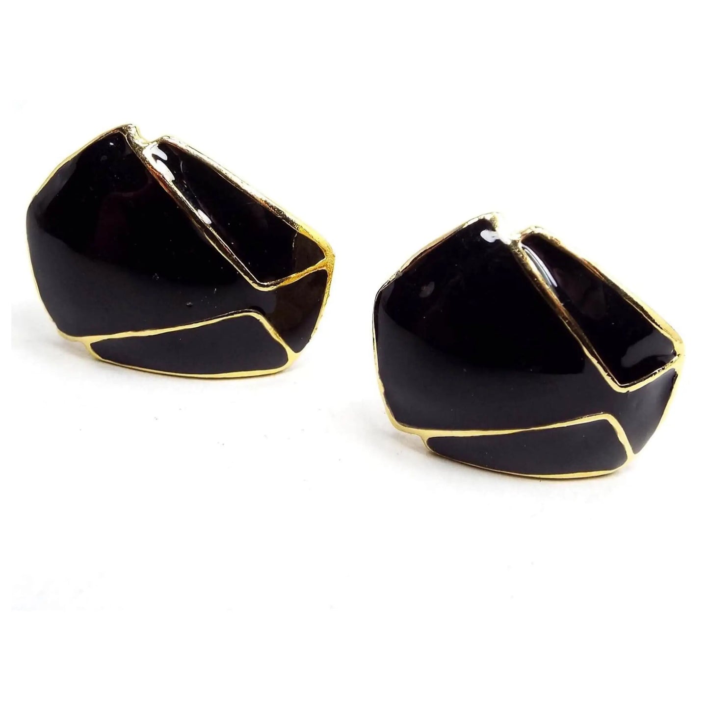 Angled front view of the retro vintage enameled earrings. The metal is gold tone in color and the enamel is black. The have a geometric style design/