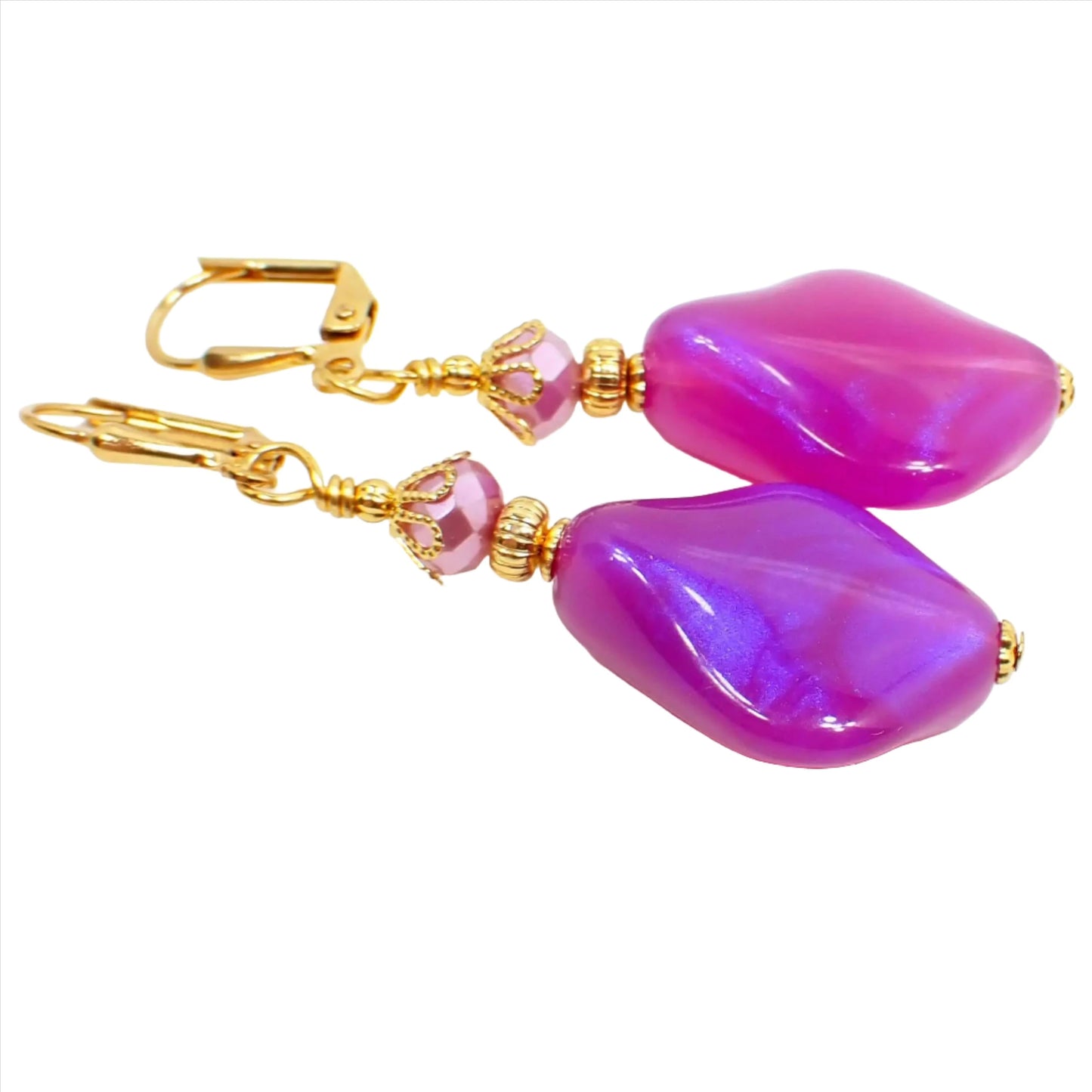 Front view of the handmade color shift purple lucite earrings. The metal is gold plated in color. There are pearly glass faceted beads at the top and angled teardrop beads at the bottom. The bottom beads have an indented curve and are bright purple in color with hints of sparkly purple as you move around.