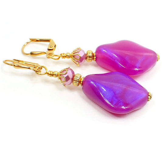 Front view of the handmade color shift purple lucite earrings. The metal is gold plated in color. There are pearly glass faceted beads at the top and angled teardrop beads at the bottom. The bottom beads have an indented curve and are bright purple in color with hints of sparkly purple as you move around.
