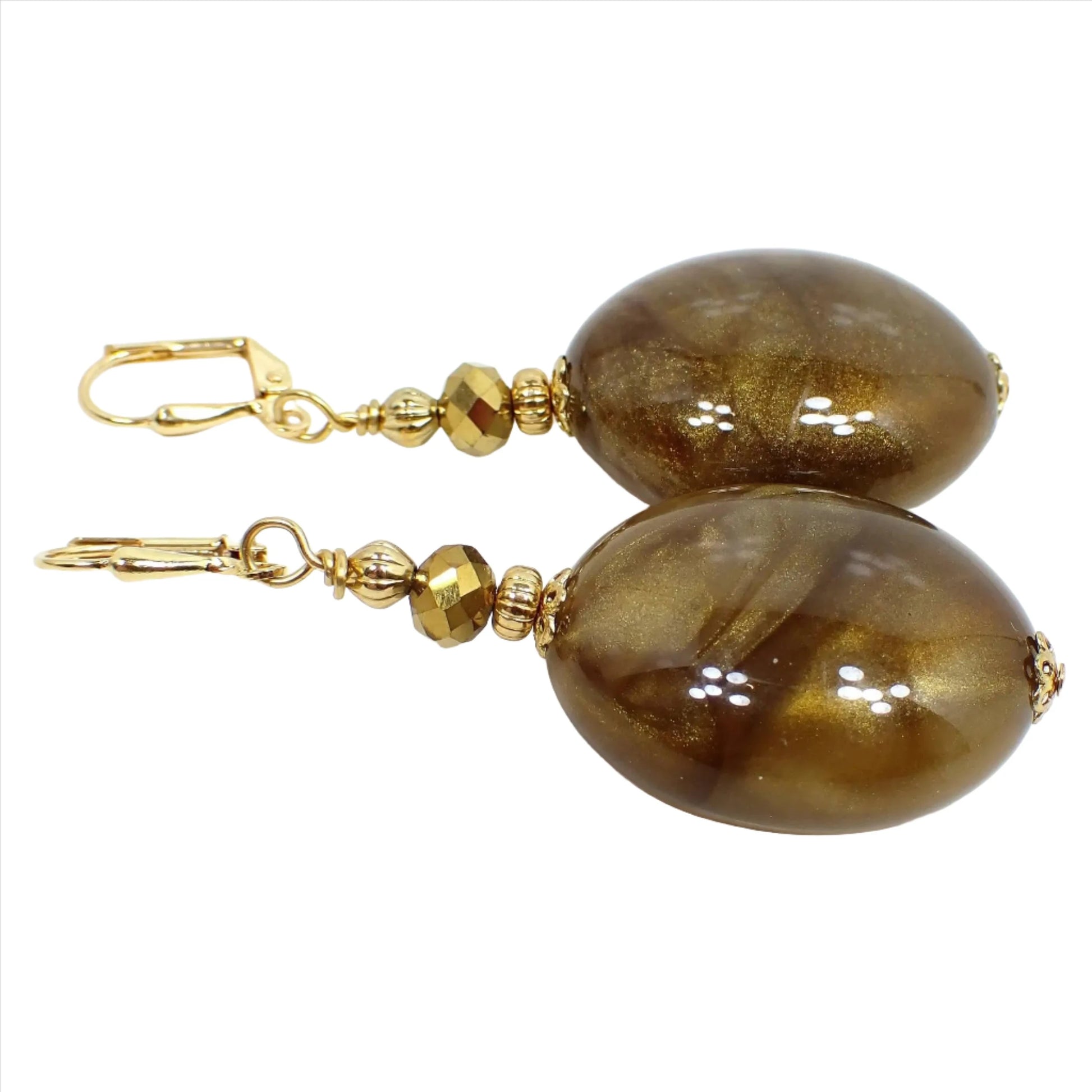 Angled view of the big oval handmade drop earrings with vintage lucite beads. The metal is gold plated in color. There are faceted metallic bronze glass beads at the top. The bottom beads are large puffy ovals that have marbled swirls in different shades of pearly golden brown.