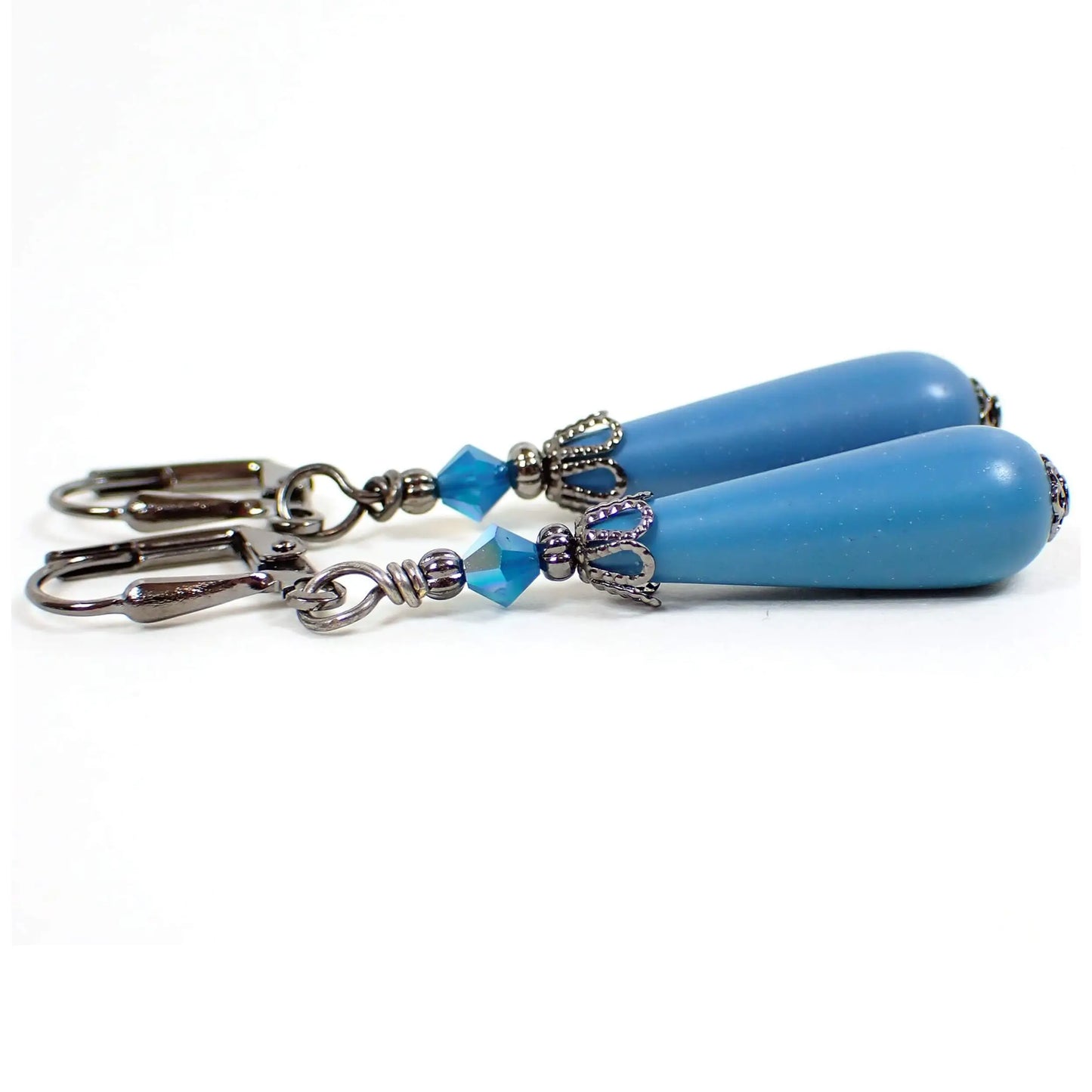 Side view of the handmade teardrop earrings with vintage lucite beads. The metal is gunmetal gray in color. There are new opaque blue faceted glass beads at the top. The bottom vintage beads are teardrop shaped and are turquoise blue color lucite.