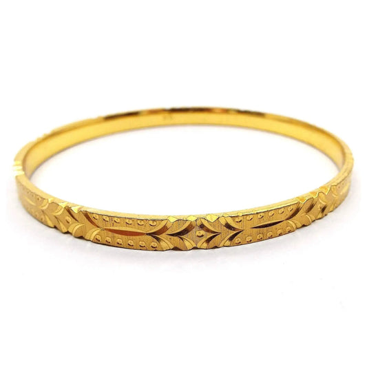 Angled side view of the Mid Century vintage Sarah Coventry bangle bracelet. It is gold tone in color with a textured tiny ridge design. There is an etched pattern of curved lines and dots all the way around the outside edge.