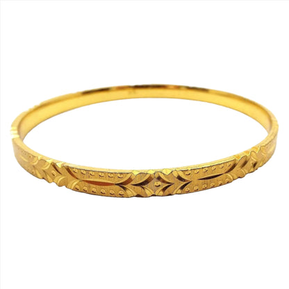 Angled side view of the Mid Century vintage Sarah Coventry bangle bracelet. It is gold tone in color with a textured tiny ridge design. There is an etched pattern of curved lines and dots all the way around the outside edge.