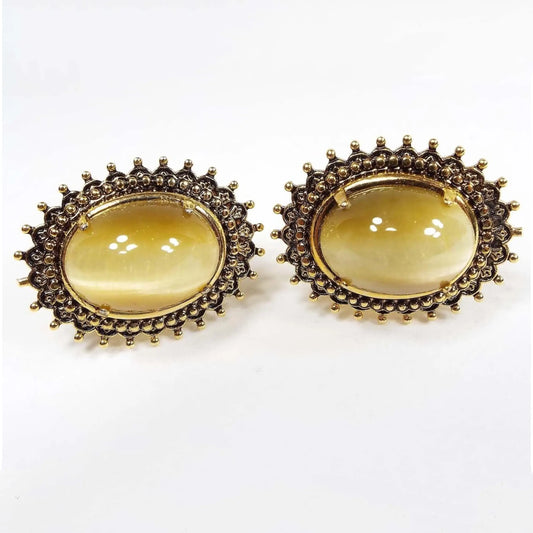 Front view of the retro vintage faux cat's eye cufflinks. The metal is oval shaped and antiqued gold in color with a spiky Brutalist style dot design. The glass cabs have shades of yellow and brown as you move around.