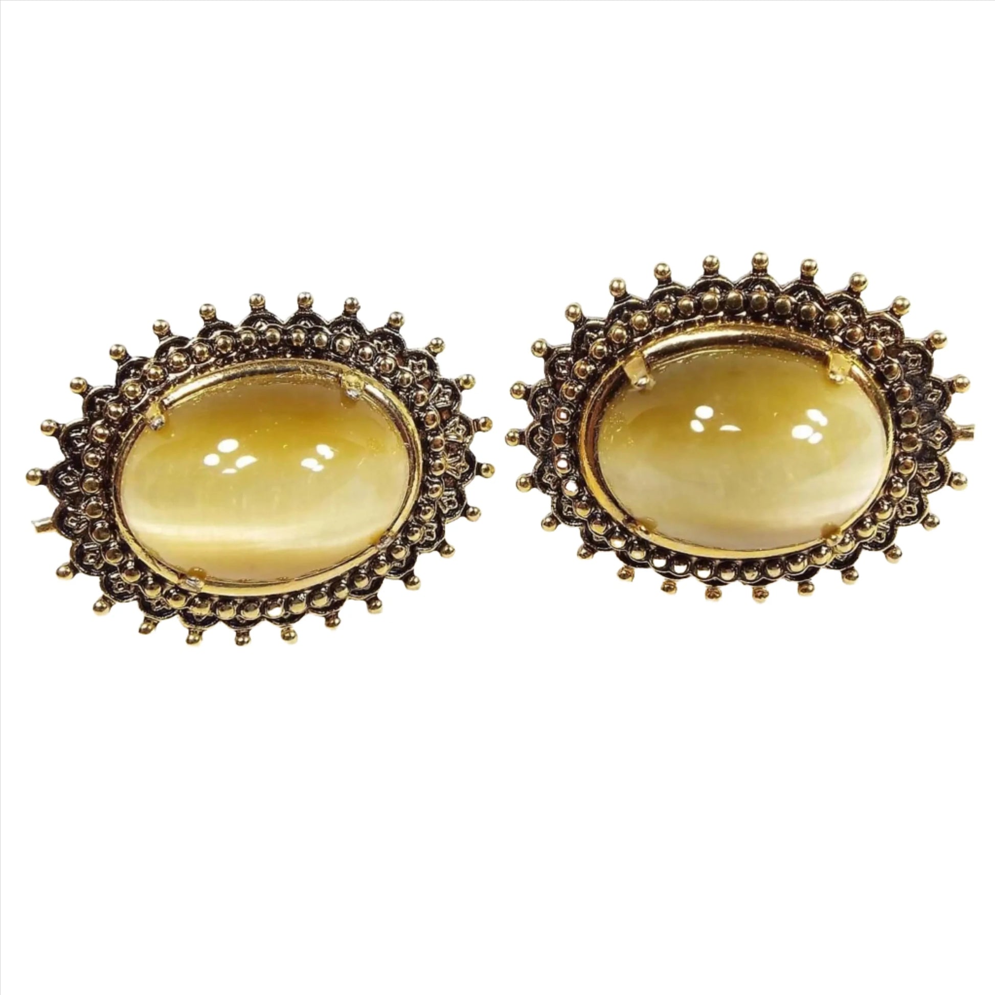 Front view of the retro vintage faux cat's eye cufflinks. The metal is oval shaped and antiqued gold in color with a spiky Brutalist style dot design. The glass cabs have shades of yellow and brown as you move around.