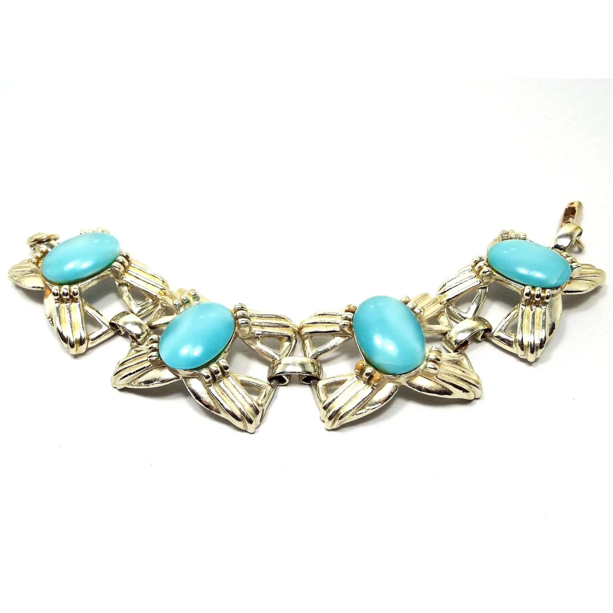 Top view of the Mid Century vintage link bracelet with glass faux cat's eye cabs. The metal is a light gold tone in color and has large bow like shaped open links. There are large oval glass cabs in aqua blue that have some flash as you move around in the light.