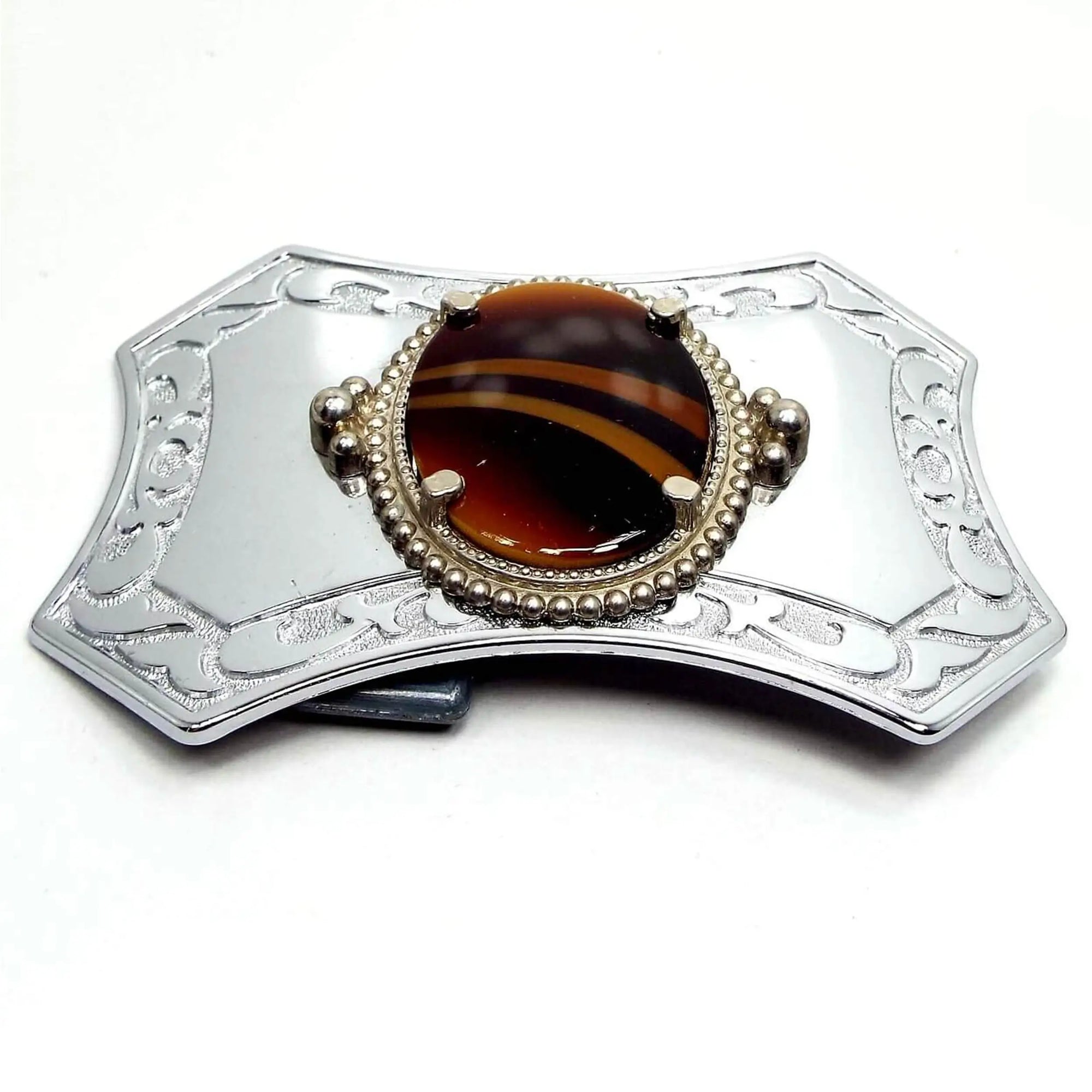 Front view of the retro vintage belt buckle with fancy glass cab. The buckle is silver tone in color and has angled out edges. There is an oval glass cab in the middle with shades of brown and hints of yellow with two angled stripes curving through the middle.