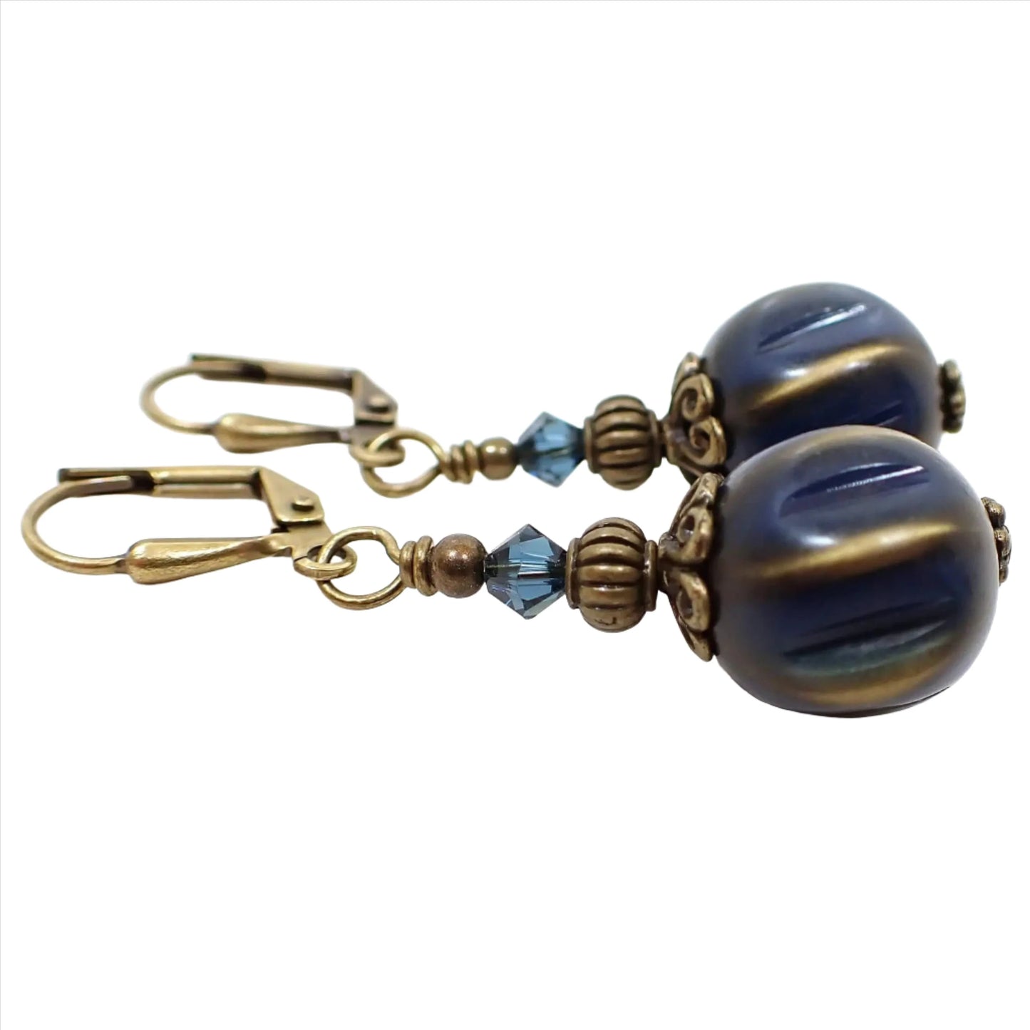 Side view of the handmade drop earrings with vintage lucite beads. The metal is antiqued brass in color. There are faceted blue glass crystals at the top. The bottom lucite beads are dark blue in color with metallic antiqued gold color accents.