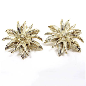 Front view of the retro vintage BSK floral earrings. They are textured gold tone in color with lots of long tapered style petals making up the flower design.