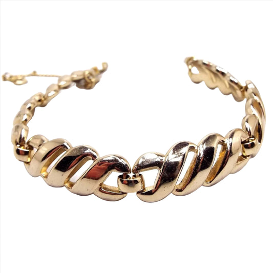 Front view of the Mid Century vintage Monet link bracelet. The metal is gold tone in color. There is a snap lock clasp and a safety chain at the end of the bracelet. The links have a curved open twist style design.