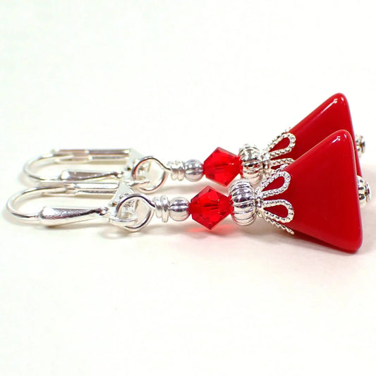 Side view of the small handmade pyramid earrings. The metal is silver plated in color. There are new red faceted glass crystal bicone beads at the top. The bottom beads are vintage lucite beads and are triangle pyramid shaped in a rich red color.