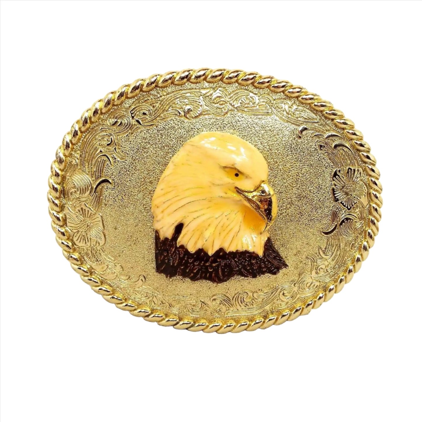 Front view of the retro vintage enameled eagle head belt buckle. The metal is gold tone in color with a floral design around the edge of the oval buckle. In the middle is an enameled bald eagle head with gold tone beak.