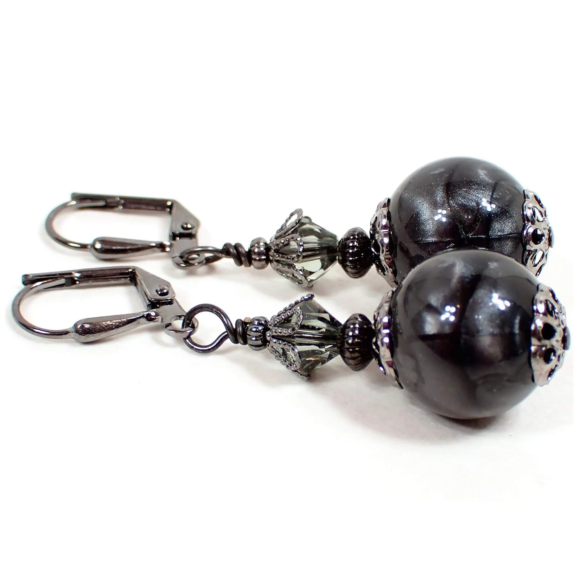 Side view of the handmade drop earrings with vintage lucite beads. The metal is gunmetal gray in color. There are smoky gray faceted glass crystal beads at the top. The lucite beads on the bottom are round sphere shaped and have a dark pearly gray color.