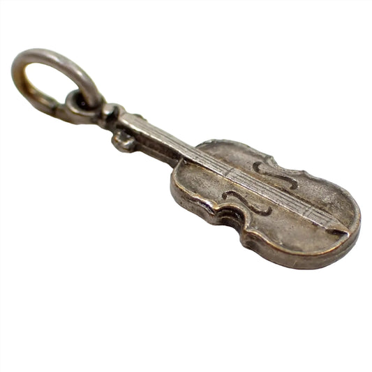 Enlarged angled view of the Mid Century vintage charm. It's shaped like a violin and is antiqued silver tone in color. There is a jump ring attached to the top.