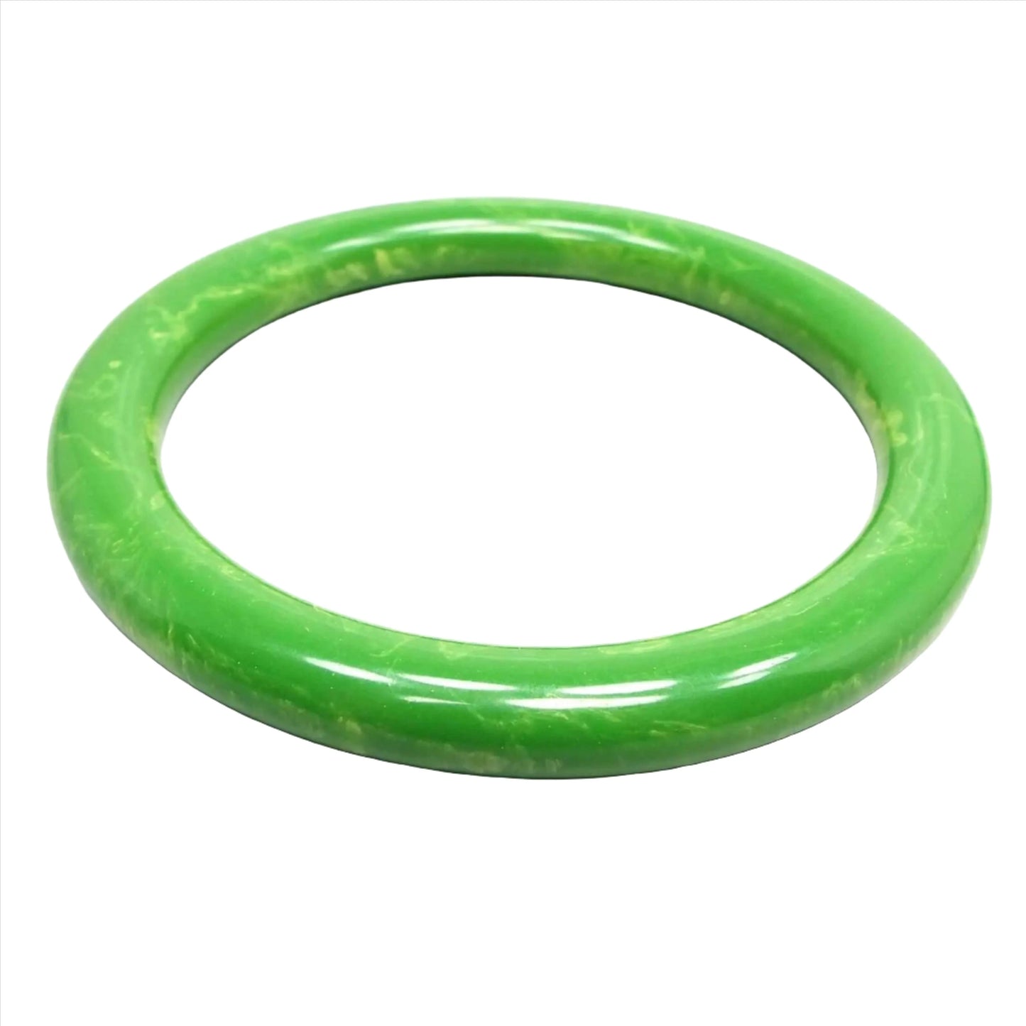 Angled top view of the 1960's vintage lucite bangle bracelet. The bangle is rounded and mostly green in color with some yellow marbled in here and there.