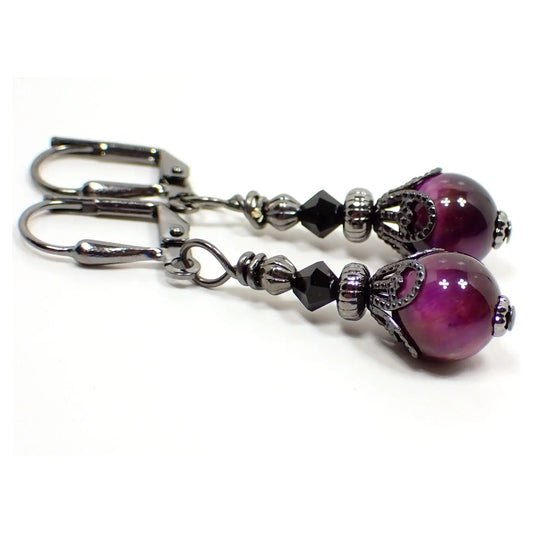 Photo of the handmade tiger's eye gemstone earrings. The metal is gunmetal gray in color. There are faceted glass black beads at the top. The bottom tiger's eye beads are small round ball shaped and are dyed a dark purple in color.