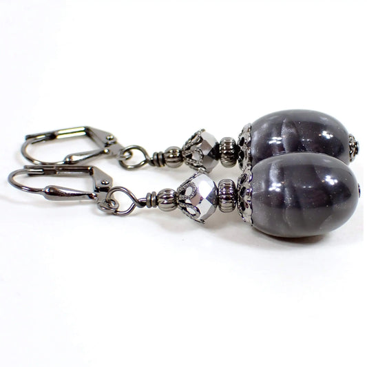 Angled view of the handmade drop earrings with vintage lucite beads. The metal is gunmetal gray in color. There are faceted metallic gray glass beads at the top. The bottom lucite beads are oval shaped and have a pearly mix of light and dark gray color.