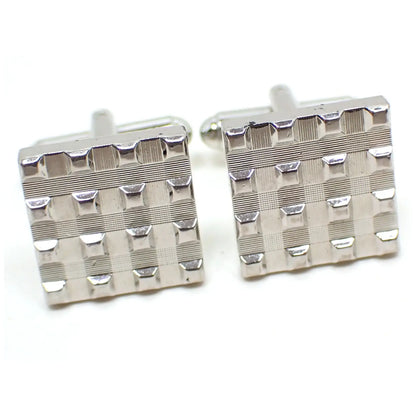 Enlarged front view of the retro vintage cufflinks. The metal is silver tone plated in color. They are square shaped and have a woven waffle like design of small squares on the front.