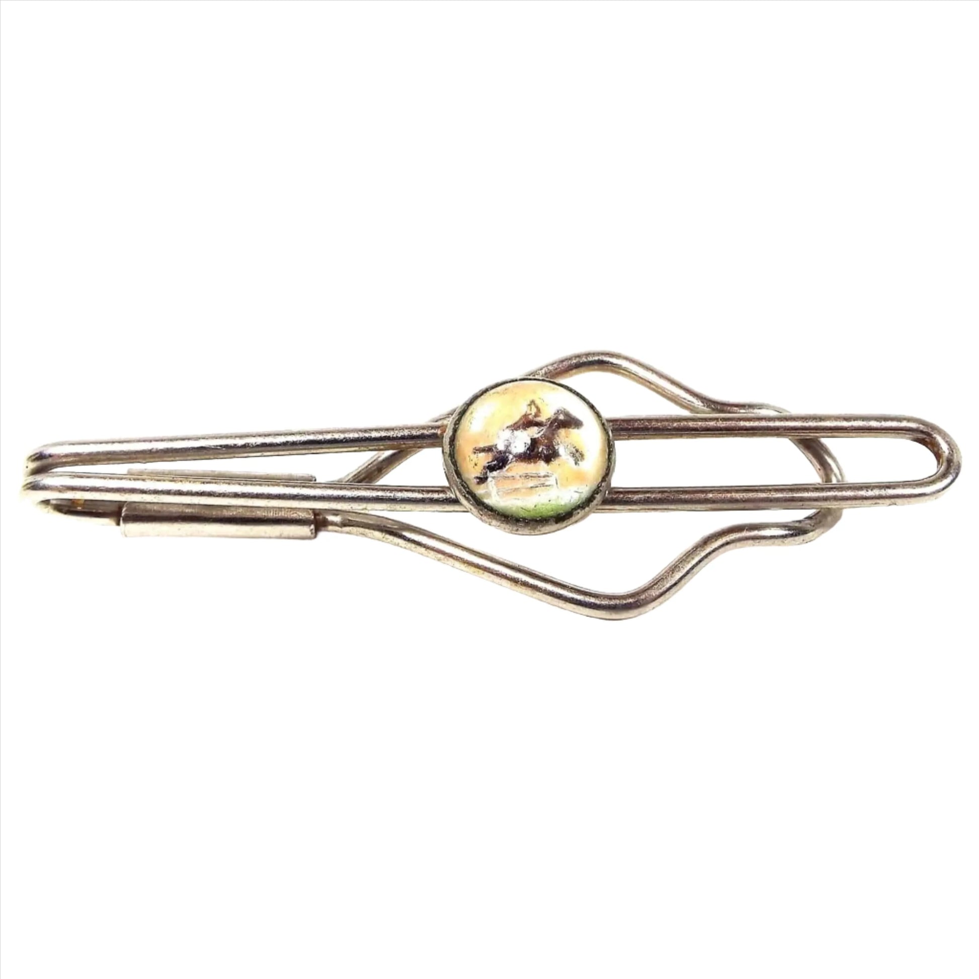 Front view of the Mid Century vintage slide on tie bar with intaglio cab. The metal is silver tone in color and has an open wire style shape. In the middle is a domed round plastic intaglio cab with a horse and rider jumping on it.