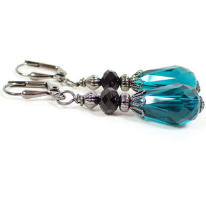 Side view of the handmade teardrop earrings. The metal is gunmetal gray in color. There are black faceted glass beads at the top and teal blue faceted glass crystal teardrop beads on the bottom.