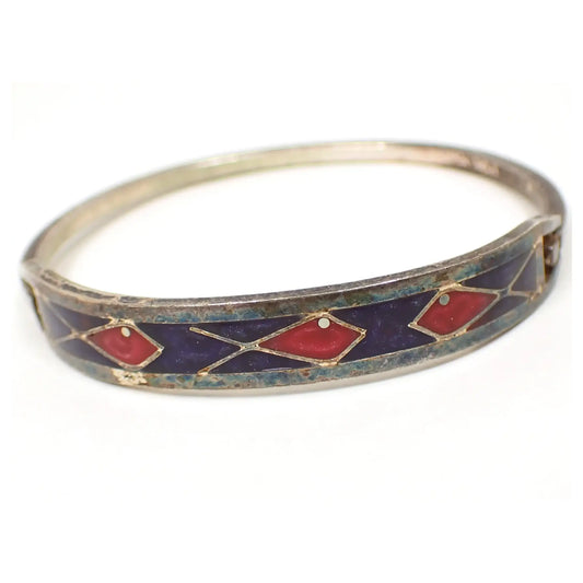Front view of the retro vintage Mexican enameled hinged bangle bracelet. The silver tone metal is very darkened in color. There is a bluish tint to some of the metal on the front when magnified under lighting. The curved bar on the front has dark blue pearly resin enamel with three pearly pink and red fish in the design.