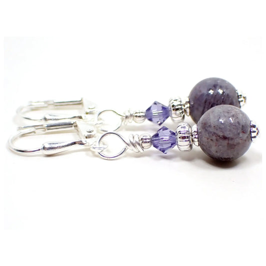 Side view of the small handmade iolite sunstone drop earrings. The metal is silver plated in color. There are faceted light purple glass crystal beads at the top. The bottom gemstone beads are small round sphere shaped and are shades of light purple in color with speckles.